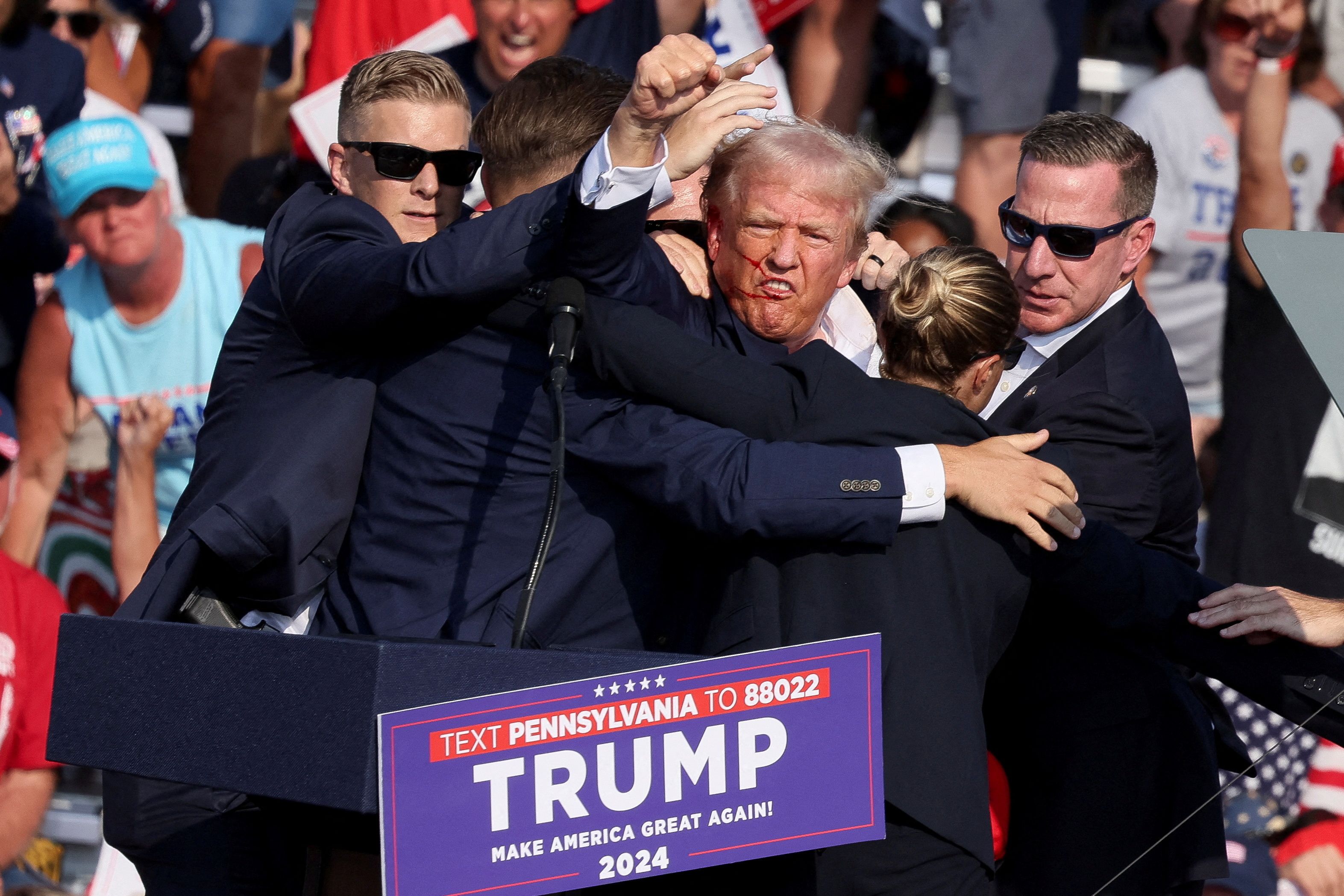 Republican presidential candidate and former US President Donald Trump gestures with a bloodied face while he is assisted by US Secret Service personnel after he was shot in the right ear during a campaign rally at the Butler Farm Show in Butler, Pennsylvania, July 13, 2024. Credit: Reuters File Photo