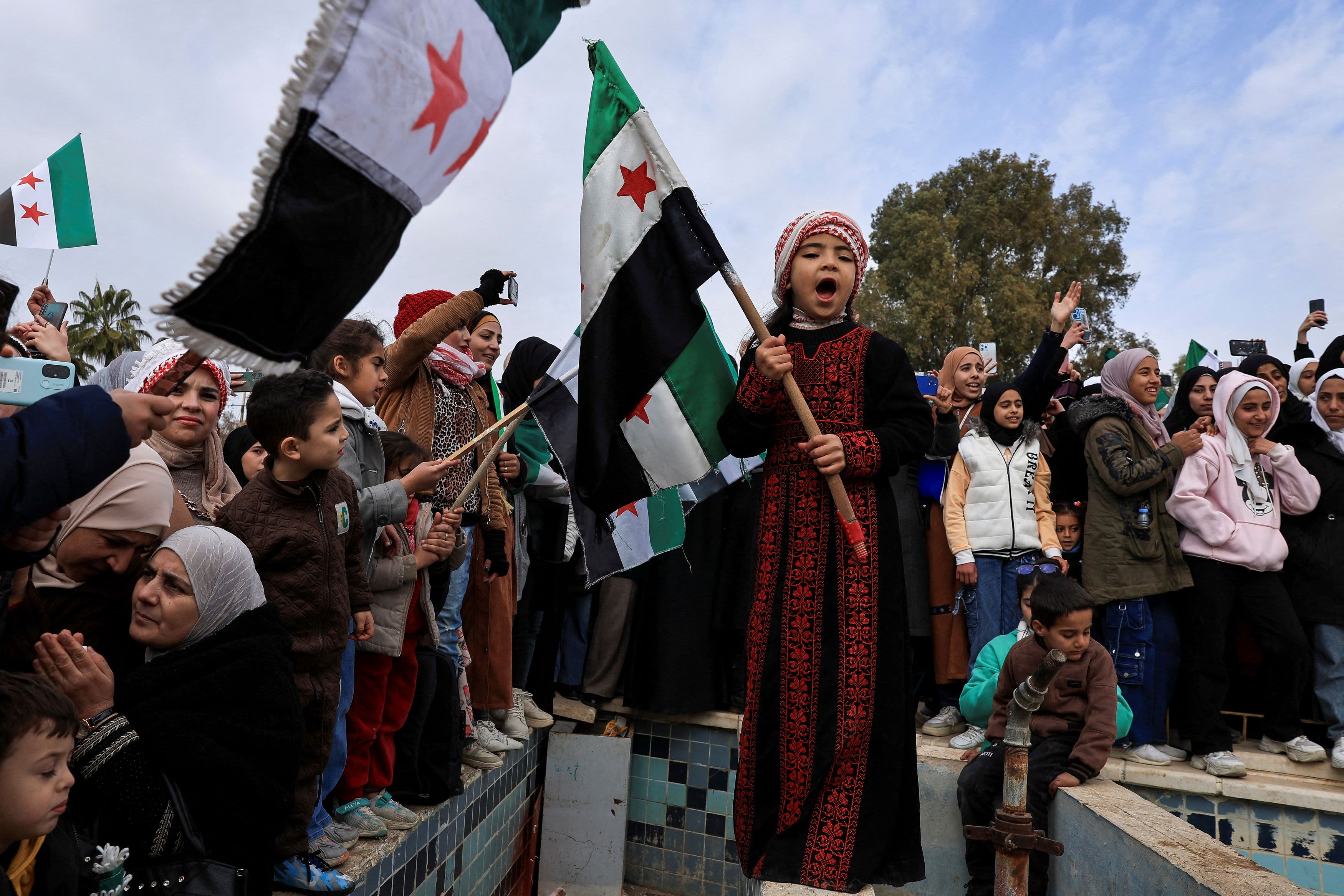 A child holds the flag adopted by the new Syrian rulers, as people gather to celebrate after the ousting of Syria's Bashar al-Assad, at March 18 Square in Daraa, Syria, December 27, 2024. Credit: Reuters Photo